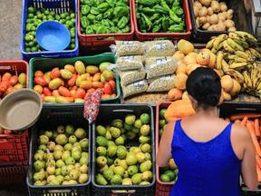 mulher de costas, de blusa azul, comprando frutas e verduras