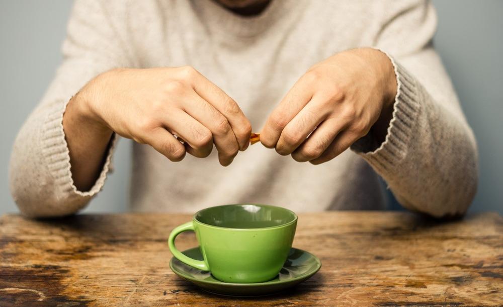Homem rasga pacote de adoçante para despejar em caneca de café