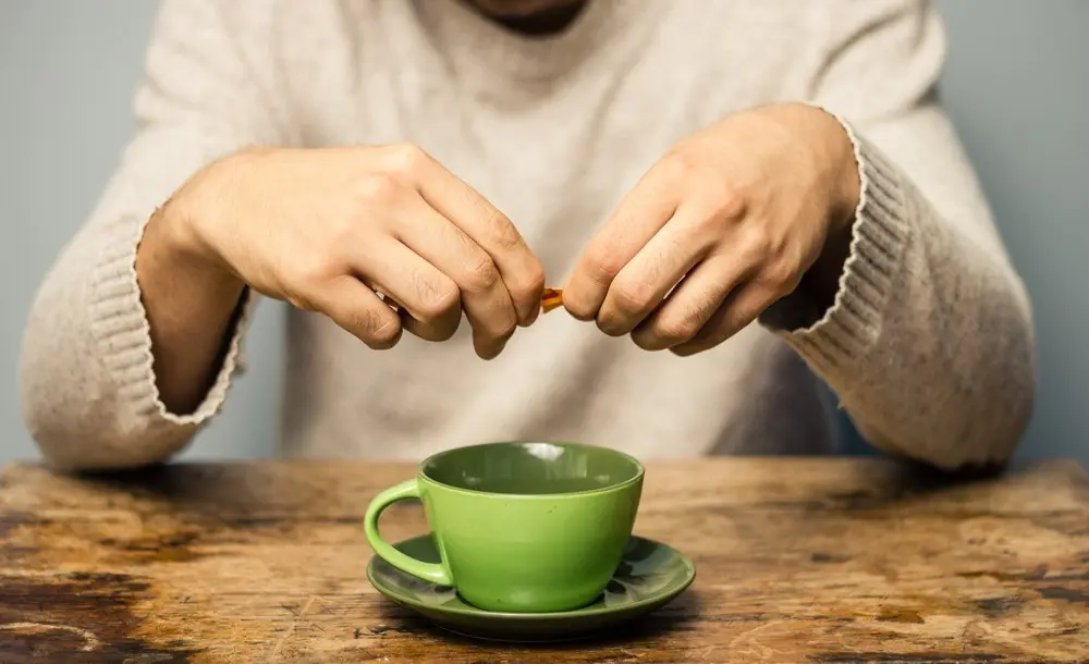 Homem rasga pacote de adoçante para despejar em caneca de café