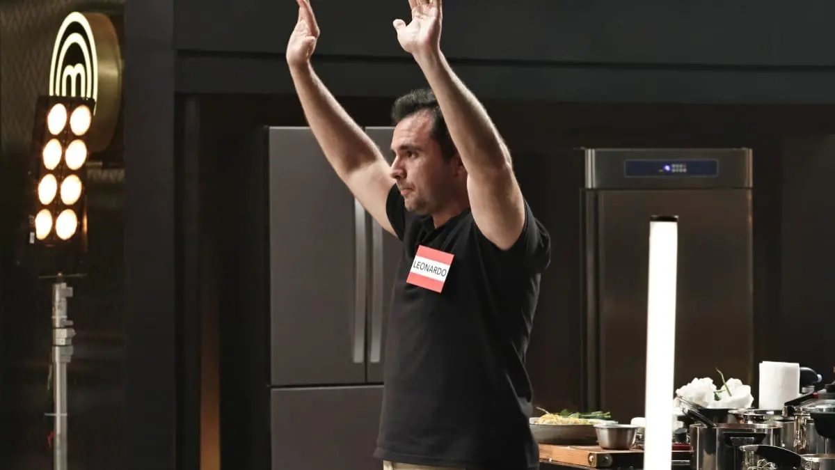 Leonardo de mãos para cima, vestindo camiseta preta, na cozinha do masterchef
