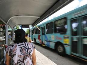 Mulher aguarda em ponto de ônibus enquanto um ônibus passa ao lado dela em alta velocidade