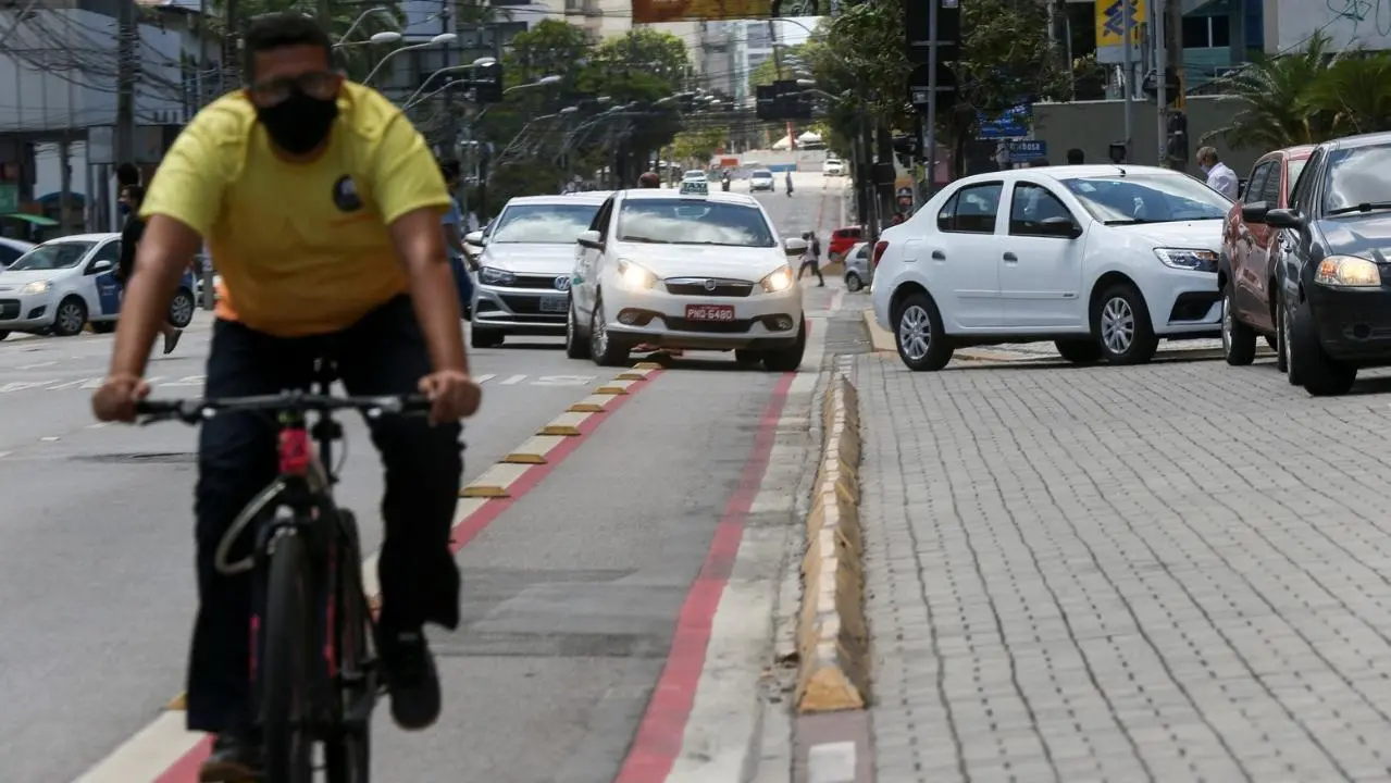 Ciclista pedala em ciclofaixa. Ao fundo, carros