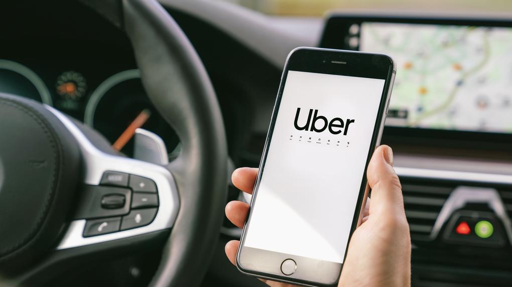 Motorista Uber segurando seu smartphone no carro. Uber é uma empresa americana que oferece diferentes serviços de transporte online