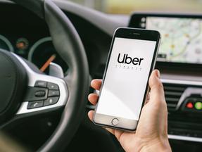 Motorista Uber segurando seu smartphone no carro. Uber é uma empresa americana que oferece diferentes serviços de transporte online