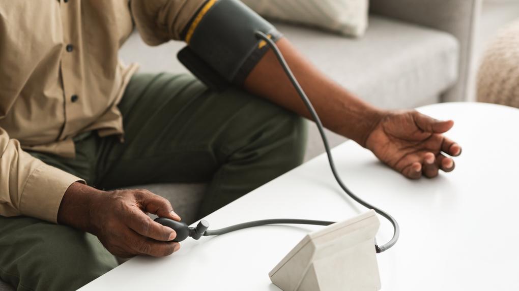 Imagem em close-up mostra pessoa negra aferindo a pressão arterial em um aparelho esfigmomanômetro