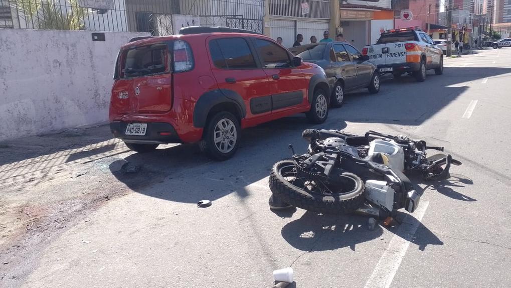 motociclista tombada no chão e carros estacionados