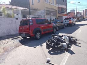 motociclista tombada no chão e carros estacionados