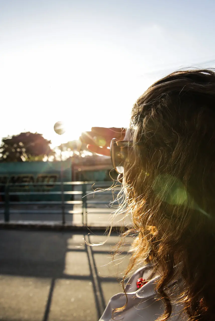 mulher de óculos escuros olhando em direção ao sol