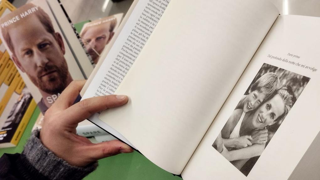pessoa abrindo livro de harry, mostrando foto de diana e harry abraçados
