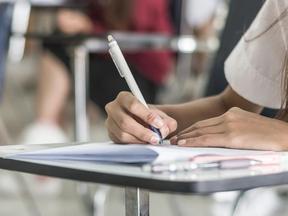 Mão de jovem escreve em papel em sala de aula