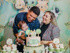 Aniversário de 1 ano do Eliseu. Pai, mãe e criança atrás de bolo e mesa decorada