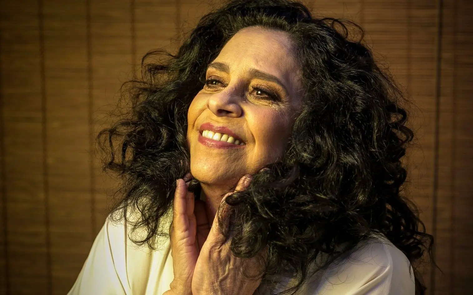 Gal Costa posa para foto de perfil. Ela está maquiada e tme vastelos cabelos pretos ondulados