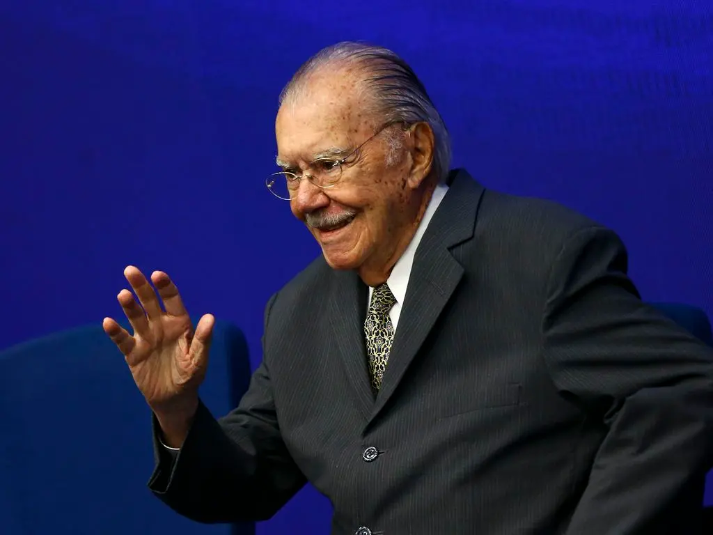 José Sarney é um homem idoso , branco, de bigode grisalho e óculos pequenos, redondos