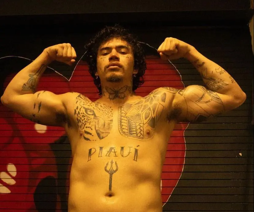 Whindersson nunes faz pose de luta. Ele está sem camisa. É um homem tatuado e de cabelo cacheado