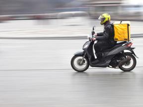 Entregador de delivery em moto atravessa pista