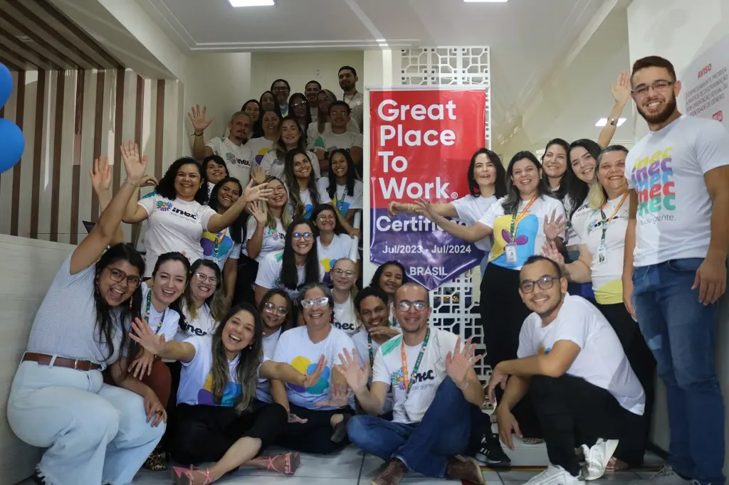 Várias pessoas estão em frente a uma placa do GPTW celebrando e comemorando