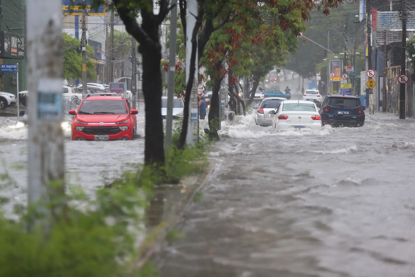 Carros e pessoa em meio a alagamento da avenida