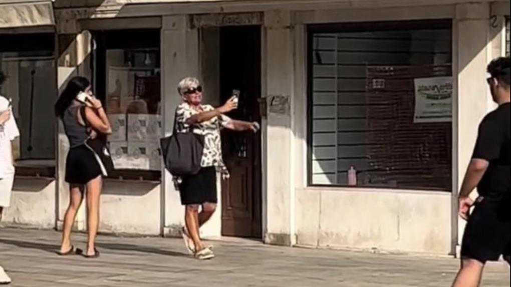 Monica caminha por calçada segurando celular