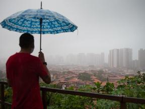 Homem sobre guarda-chuva observa cidade enevoada de Fortaleza em dia de chuva
