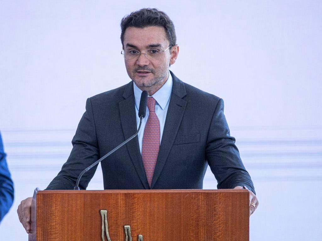 O ministro Celso Sabino é um homem branco, de barba rala, grisalha, e cabelo também grisalho. Na foto, ele está de terno, camisa branca e gravata rosa