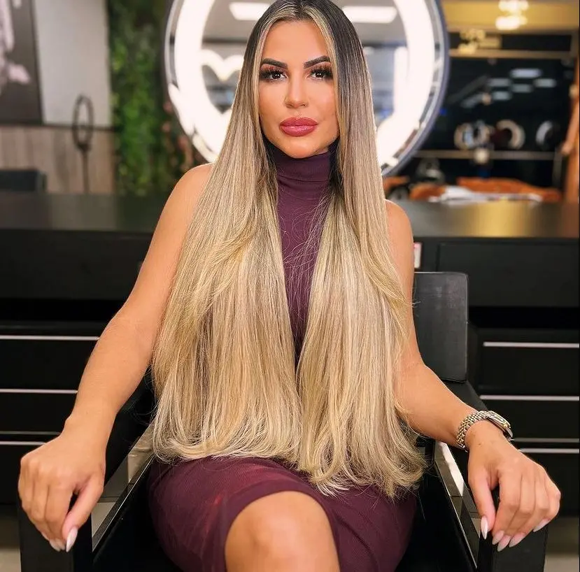 Deolane tem longos cabelos lisos e loiros. Ela é uma mulher branca e está maquiada