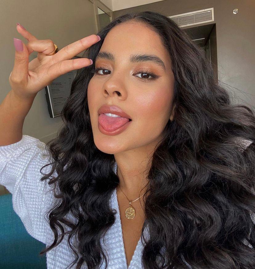 Bella Campos tem longos cabelos pretos e ondulados e está fazendo careta na foto