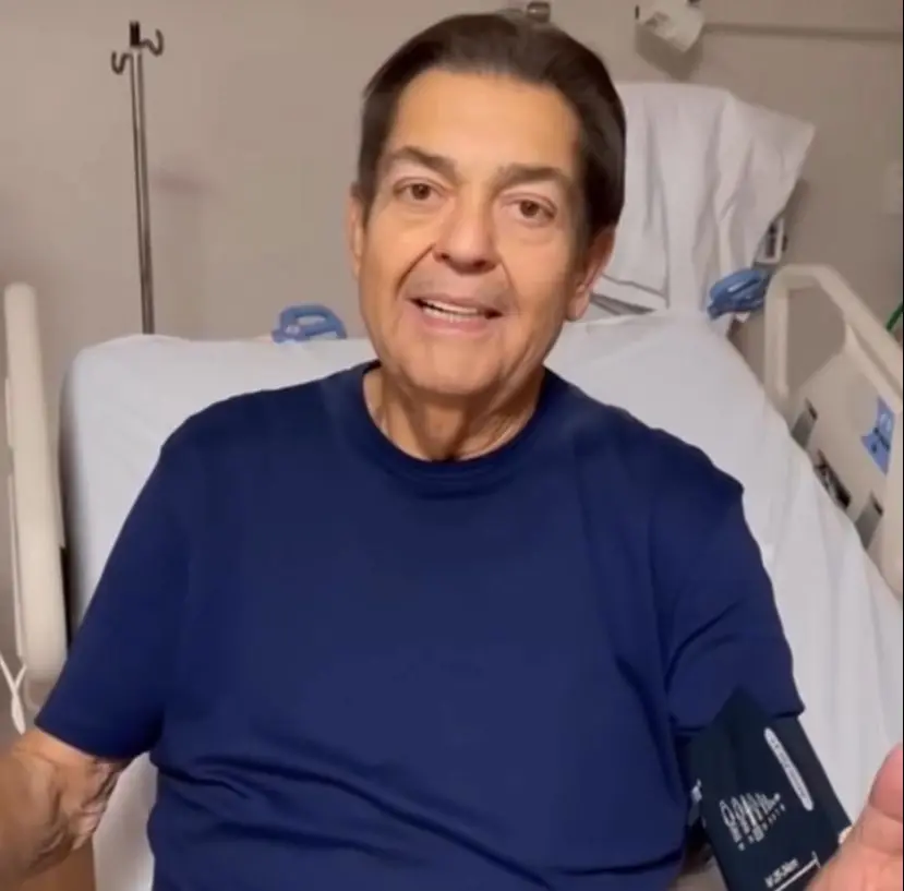 Faustão está numa maca em um hospital. Ele veste uma camisa azul