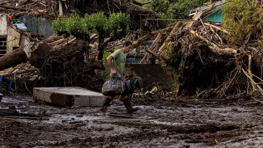 homem carrega mala em meio a destroços após enchente no rio grande do sul