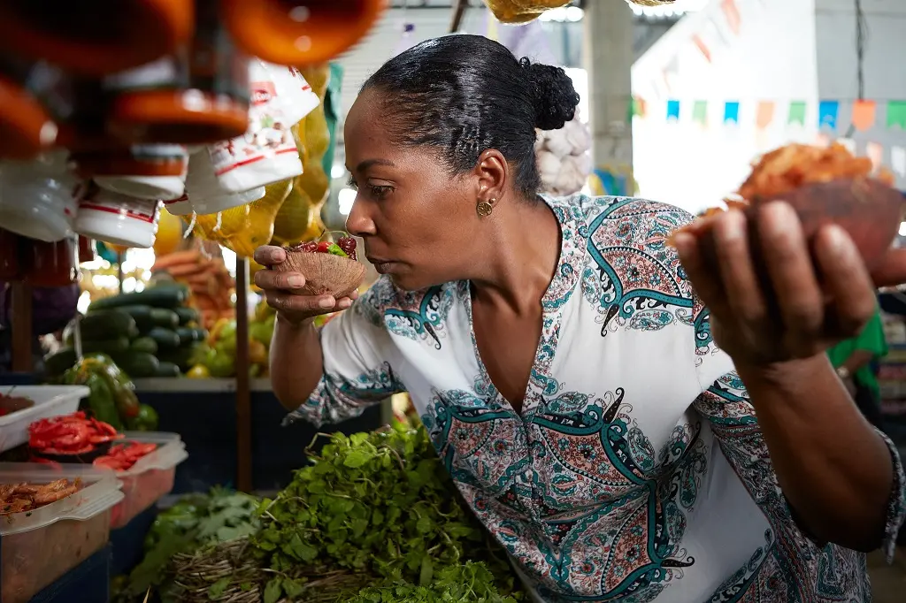 Mulher negra de cabelo em coque cheira um pote com frutas em uma feira
