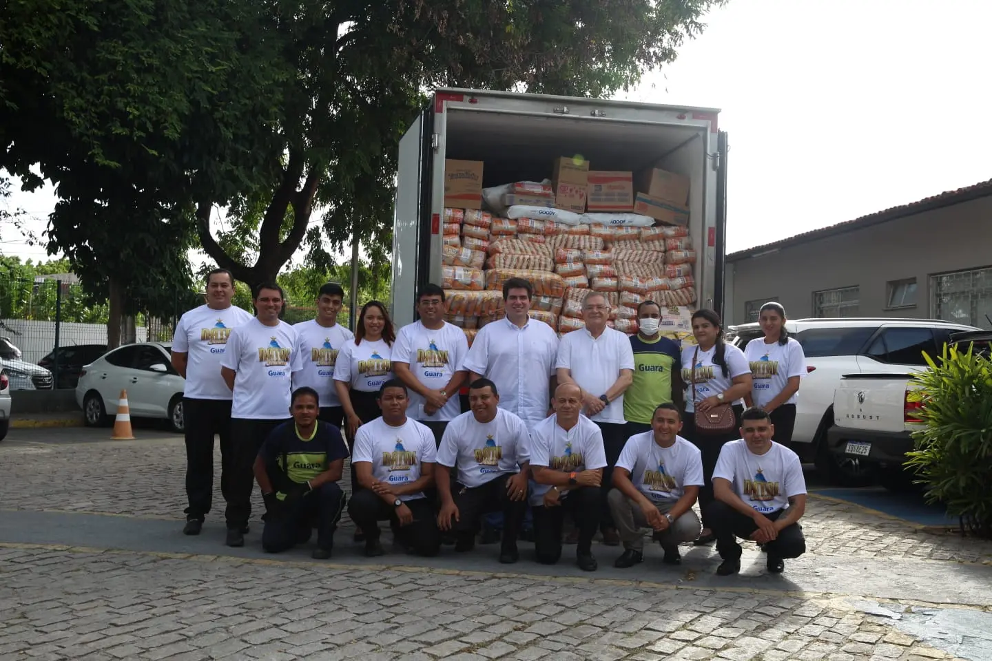 Várias pessoas reunidas em frente a um caminhão com alimentos para distribuição. Elas se alternam entre pessoas em pé e agachadas