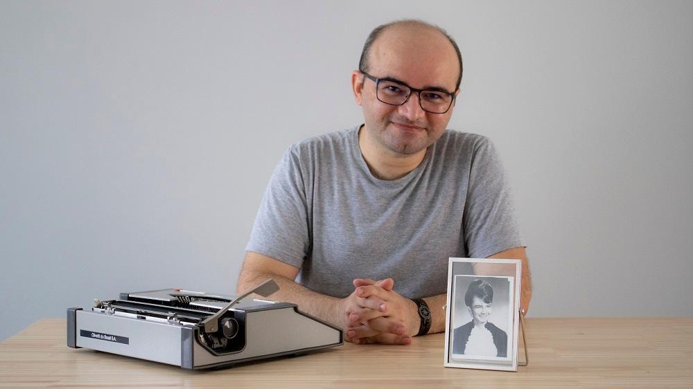 Escritor Stênio Gardel posa ao lado de uma máquina de escrever e de um retrato de mulher em preto e branco