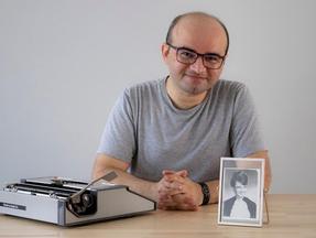 Escritor Stênio Gardel posa ao lado de uma máquina de escrever e de um retrato de mulher em preto e branco