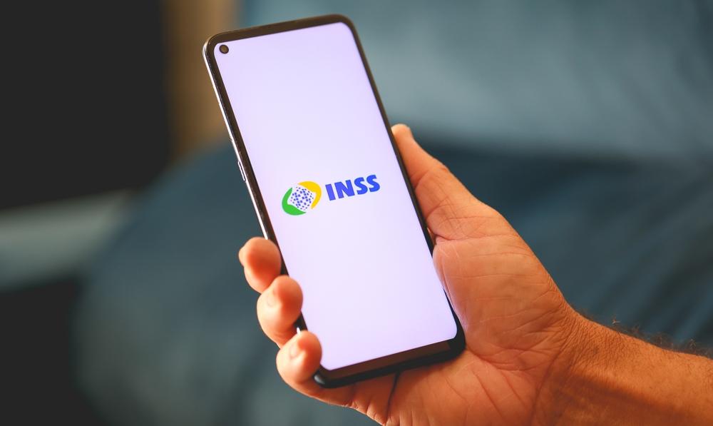 Mão segura celular com aplicativo do INSS aberto