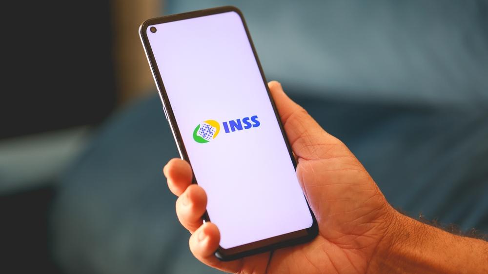 Mão segura celular com aplicativo do INSS aberto