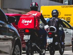Imagem mostra entregador de aplicativo entre carros e motos de rua movimentada