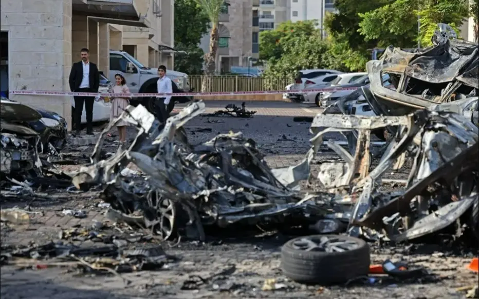 Moradores observam destroços de veículos destruídos em Ashkelon após um ataque de foguete da Faixa de Gaza ao sul de Israel em 7 de outubro de 2023 — Foto: AHMAD GHARABLI / AFP
