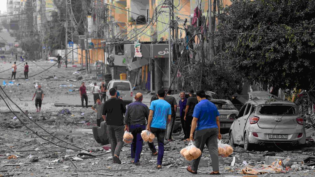 Homens palestinos carregam pão por uma rua fortemente bombardeada após ataques aéreos israelenses na Cidade de Gaza