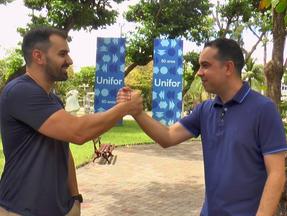 Os apresentadores Marcos Montenegro e Antero Neto seguram as mãos em frente ao campus da Unifor