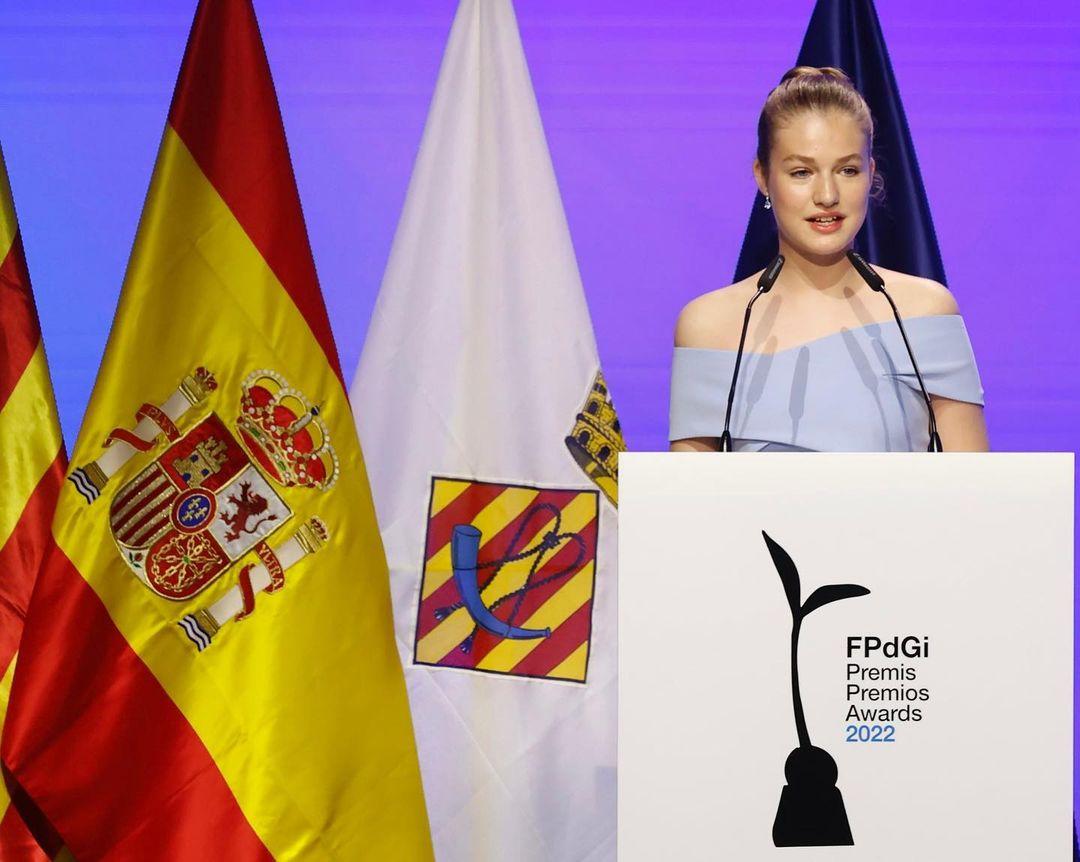 Princesa Leonor de Borbón é uma jovem branca de cabelos loiros presos. Ela está discursando e usa um vestido azul claro