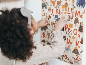 Criança negra vendo mural com imagens de letras e animais