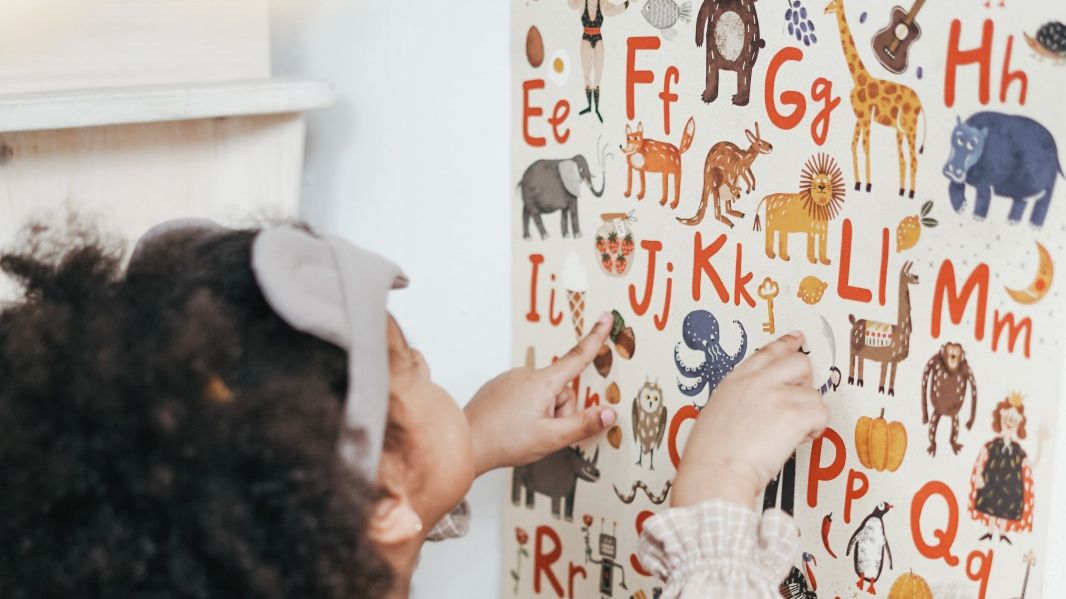 Criança negra vendo mural com imagens de letras e animais
