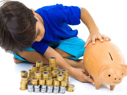 Criança brinca com cofre-porquinho e pilhas de moedas