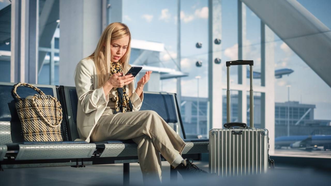 Mulher em sala de embarque de aeroporto olha descontente para celular