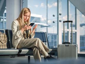 Mulher em sala de embarque de aeroporto olha descontente para celular