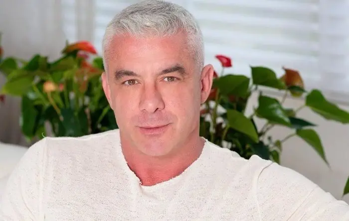 Alexandre é um homem branco e de cabelo curto, também branco. Na foto, ele está sorrindo e de camisa branca