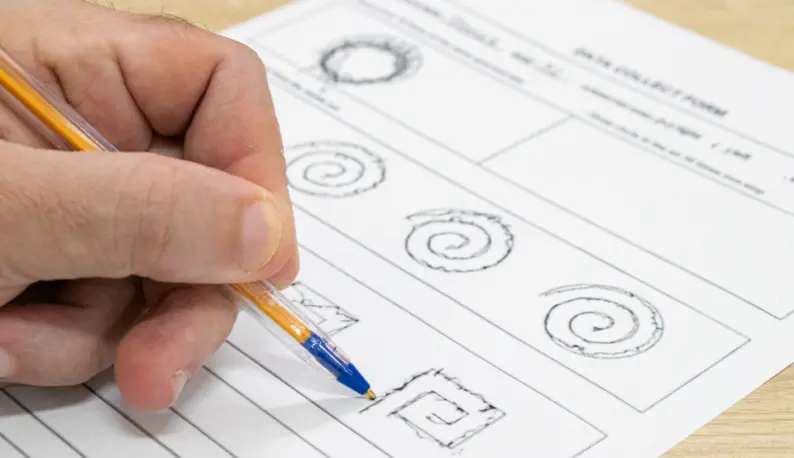 Mão de pessoa desenhando formas geométricas no teste de diadococinesia em papel