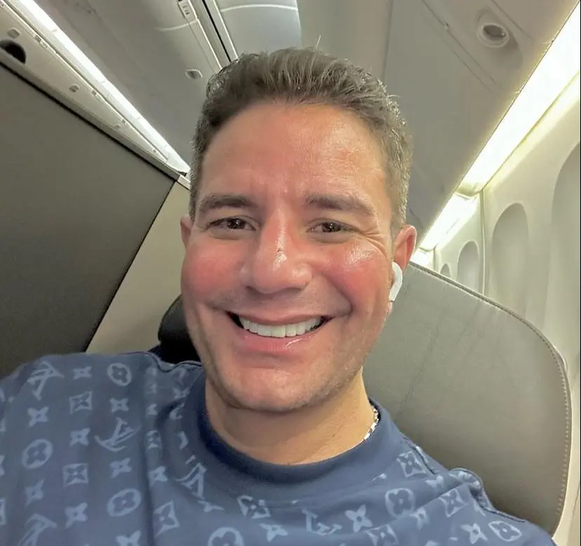 Gladson é um homem branco, loiro, de cabelo curto. Na foto, ele está sorrindo e usa fones sem fio