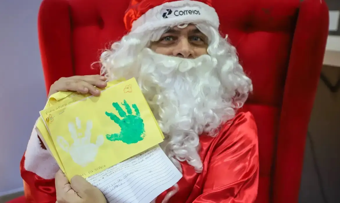 Homem vestido de papai noel segura carta recebida pelos correios