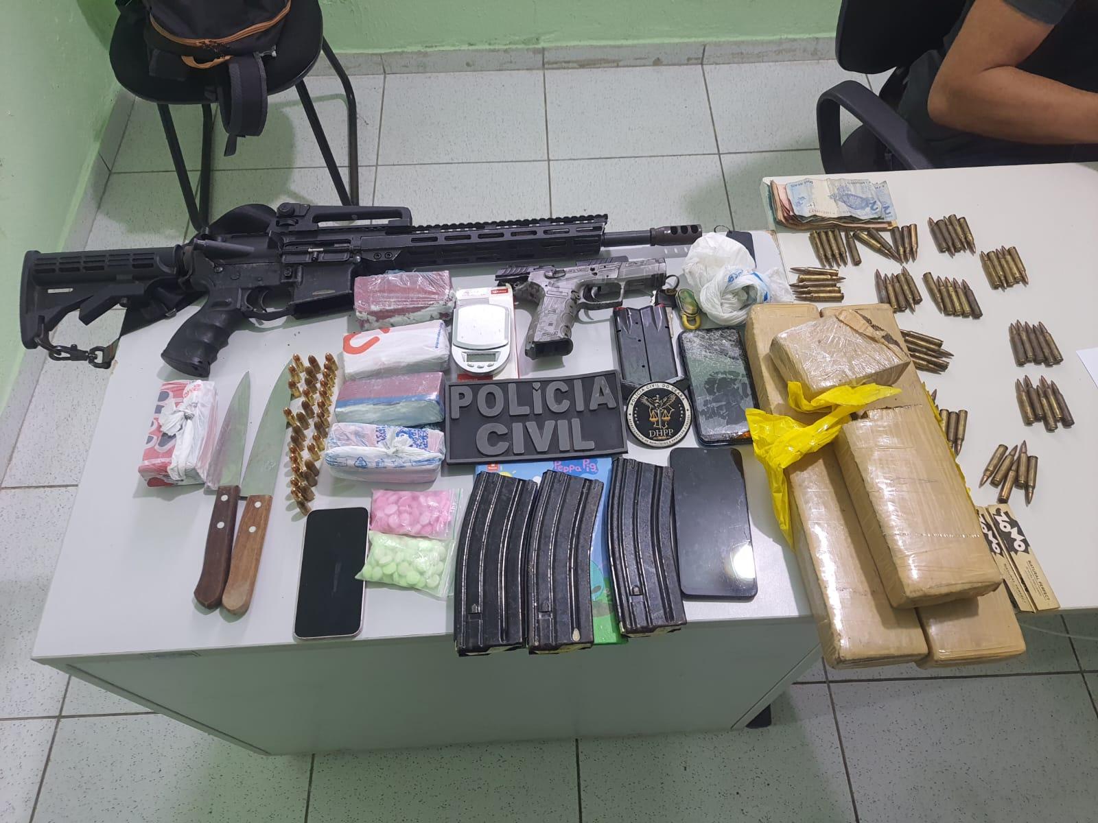 mesa com itens apreendidos: fuzil, pistola, munições, drogas e dinheiros