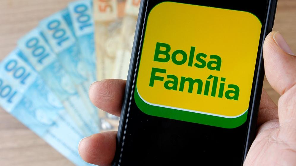 Aplicativo do Bolsa Família em cima de cédulas de 100 e 50 reais